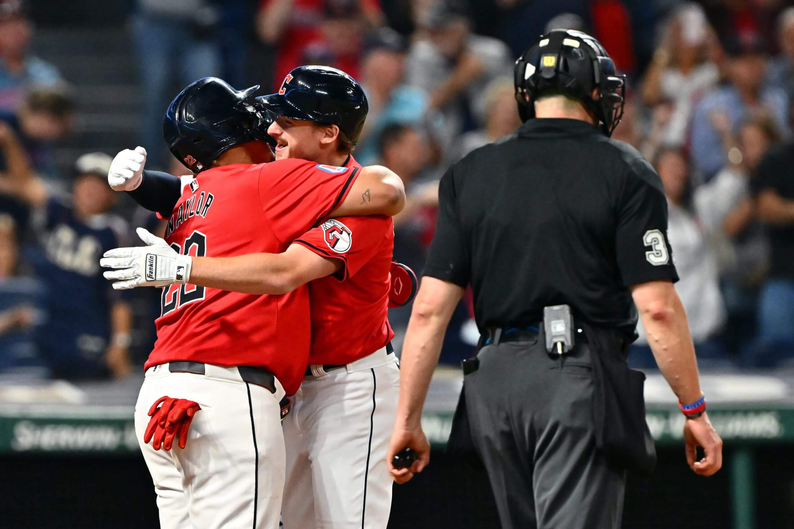 Josh Naylor and Kyle Manzardo embrace at home plate as an umpire walks by.