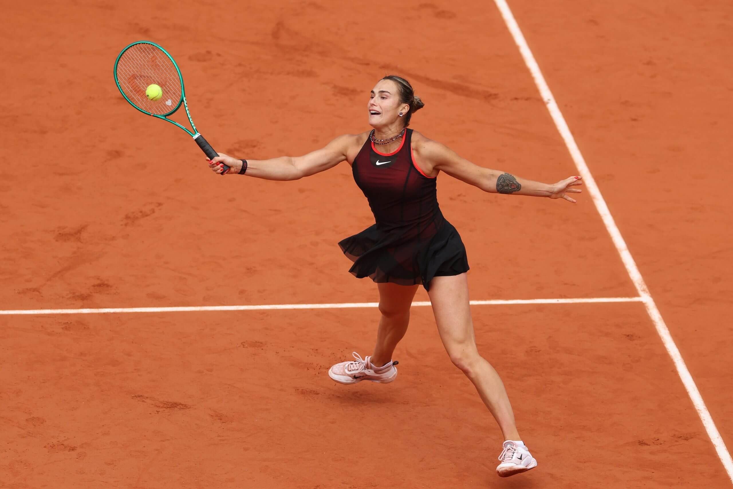 Aryna Sabalenka hits a high forehand volley on a clay tennis court.