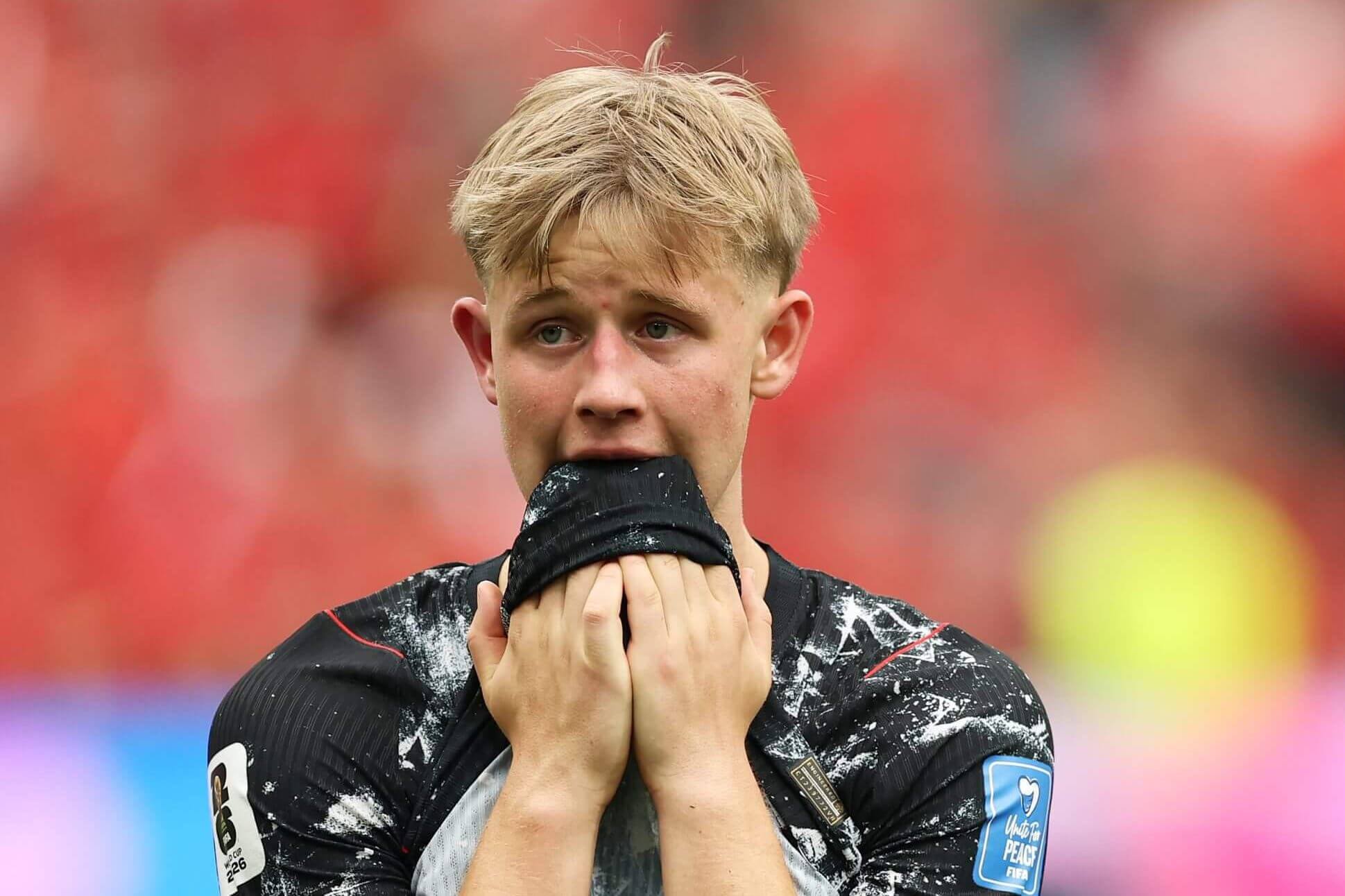 A young footballer holds his shirt in his mouth and looks upset