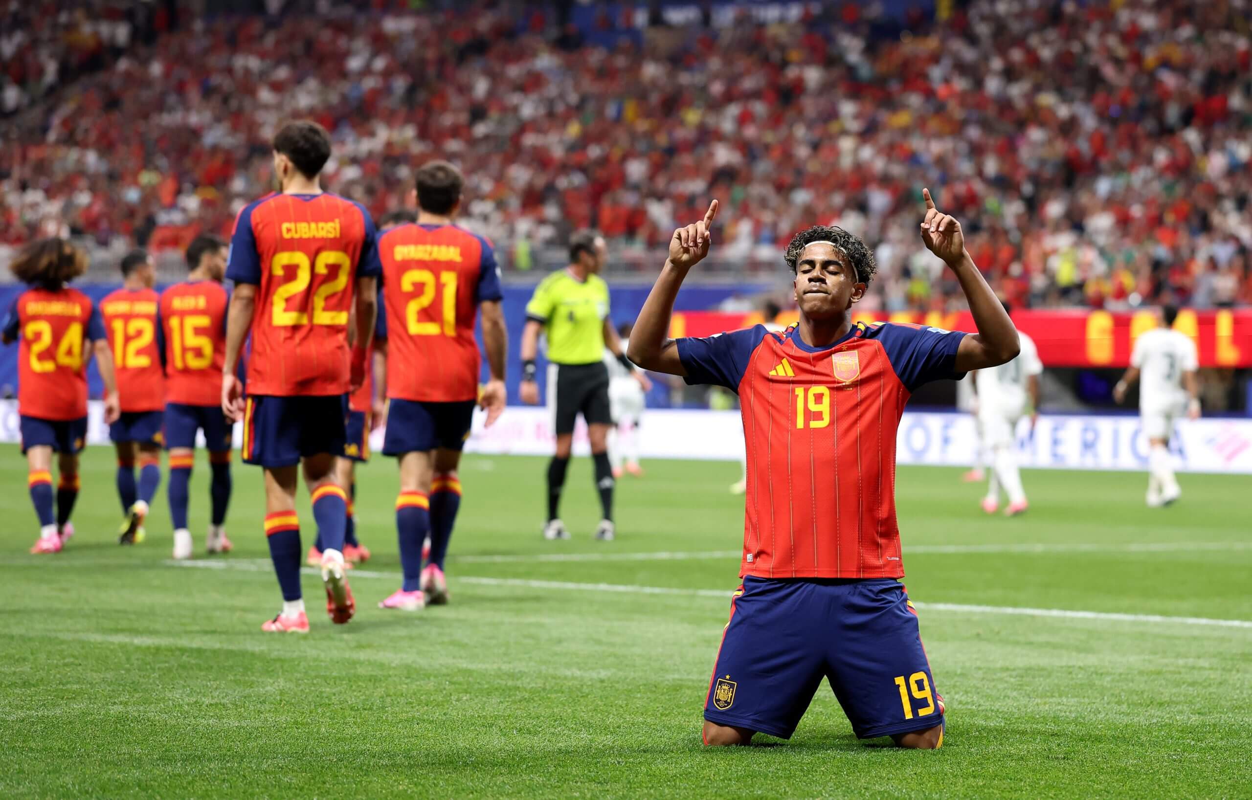 Lamine Yamal kneels on the pitch and puts both hands in the air in celebration