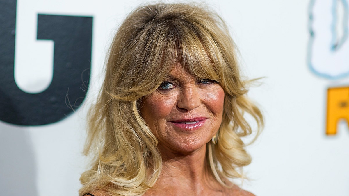 Goldie Hawn looking off-camera with bouncy blonde hair on a red carpet in New York City