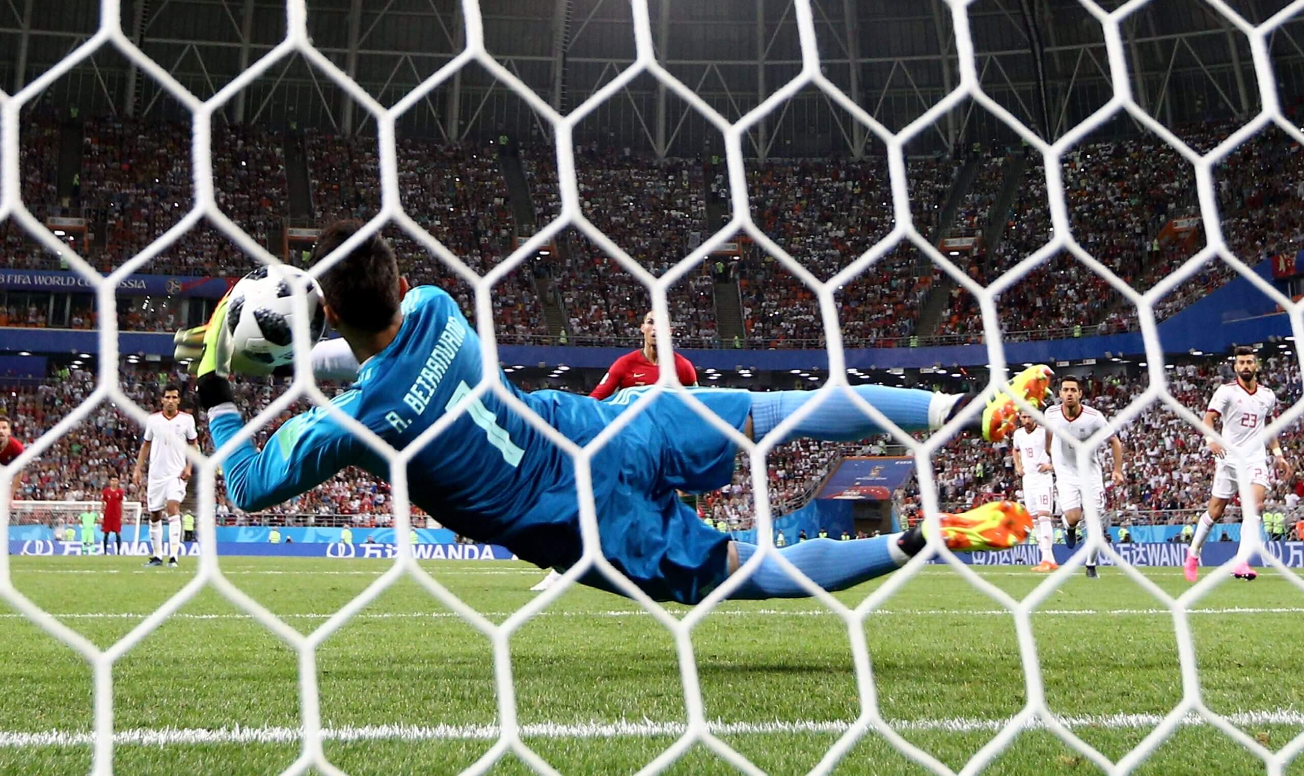 A goalkeeper in blue dives to his left to save a penalty