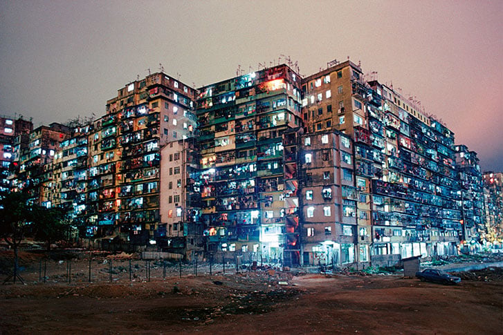 A mass of conjoined apartment buildings, pictured from the street level, at night.