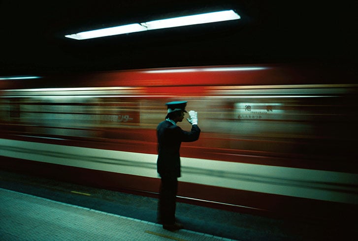 Conductor stands on a platform, as a train whizzes past.