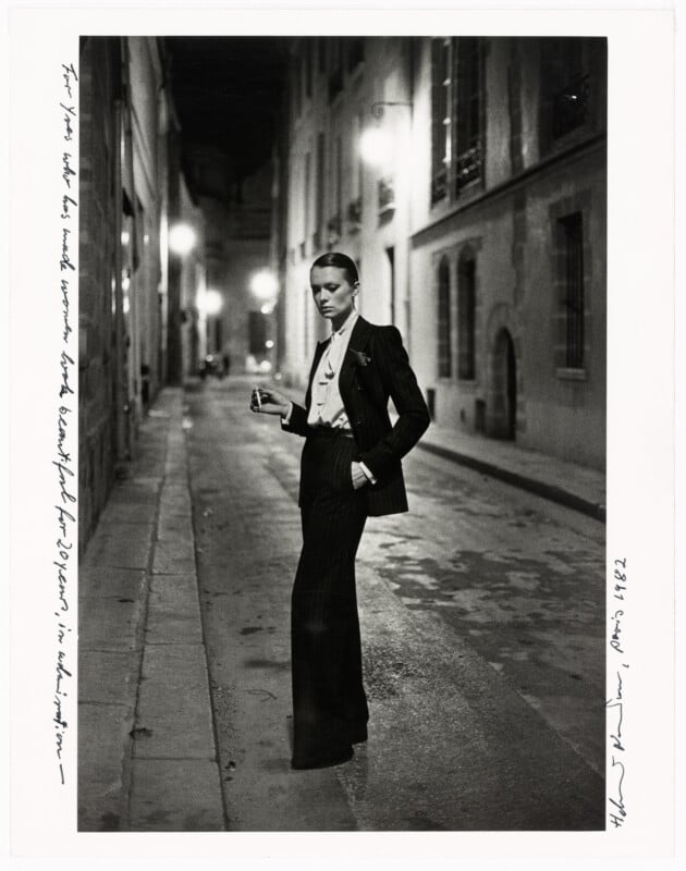 A person in a pinstripe suit and bow tie stands confidently in the middle of a dimly lit, empty city street at night, holding a cigarette. Handwritten notes frame the image on two edges.