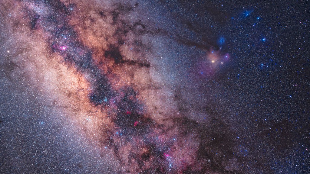 a rich cluster of stars band through the sky as the milky way fills the image, to the right is a bright red star Antares and the constellation Scorpius
