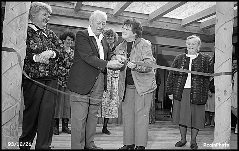 A black and white photo shows four people cutting a ribbon.