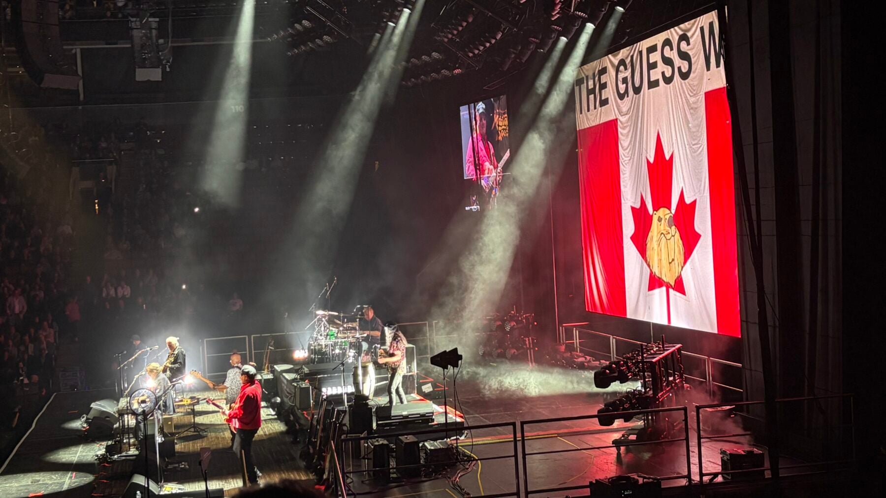 A vibrant concert stage in Toronto featuring musicians performing under bright lights, with a large Canadian flag displayed on a screen in the background, capturing the lively music scene.