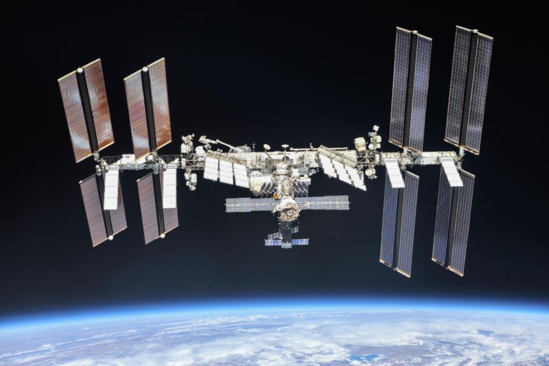 ISS leak: Space station made of linked cylinders with 4 huge solar panels at each end floating above Earth.