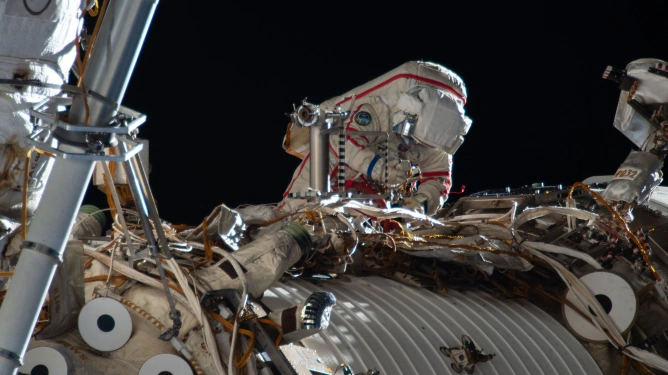 Outside the International Space Station, a space-suited cosmonaut works on something.