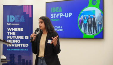 A woman speaking into a microphone in front of an IDEA Mississauga sign
