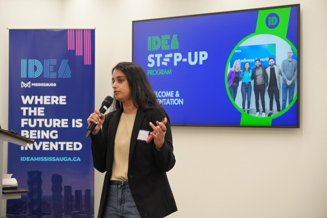 A woman speaking into a microphone in front of an IDEA Mississauga sign