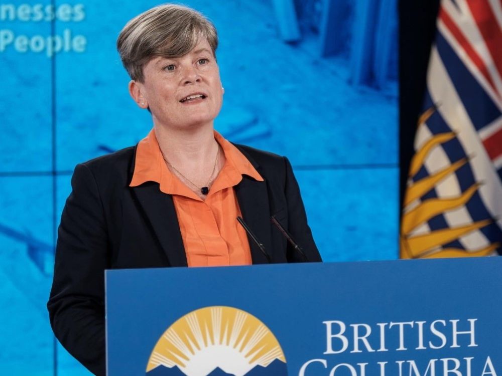 Health Minister Josie Osborne, a light-skinned woman with short hair, stands at a podium.