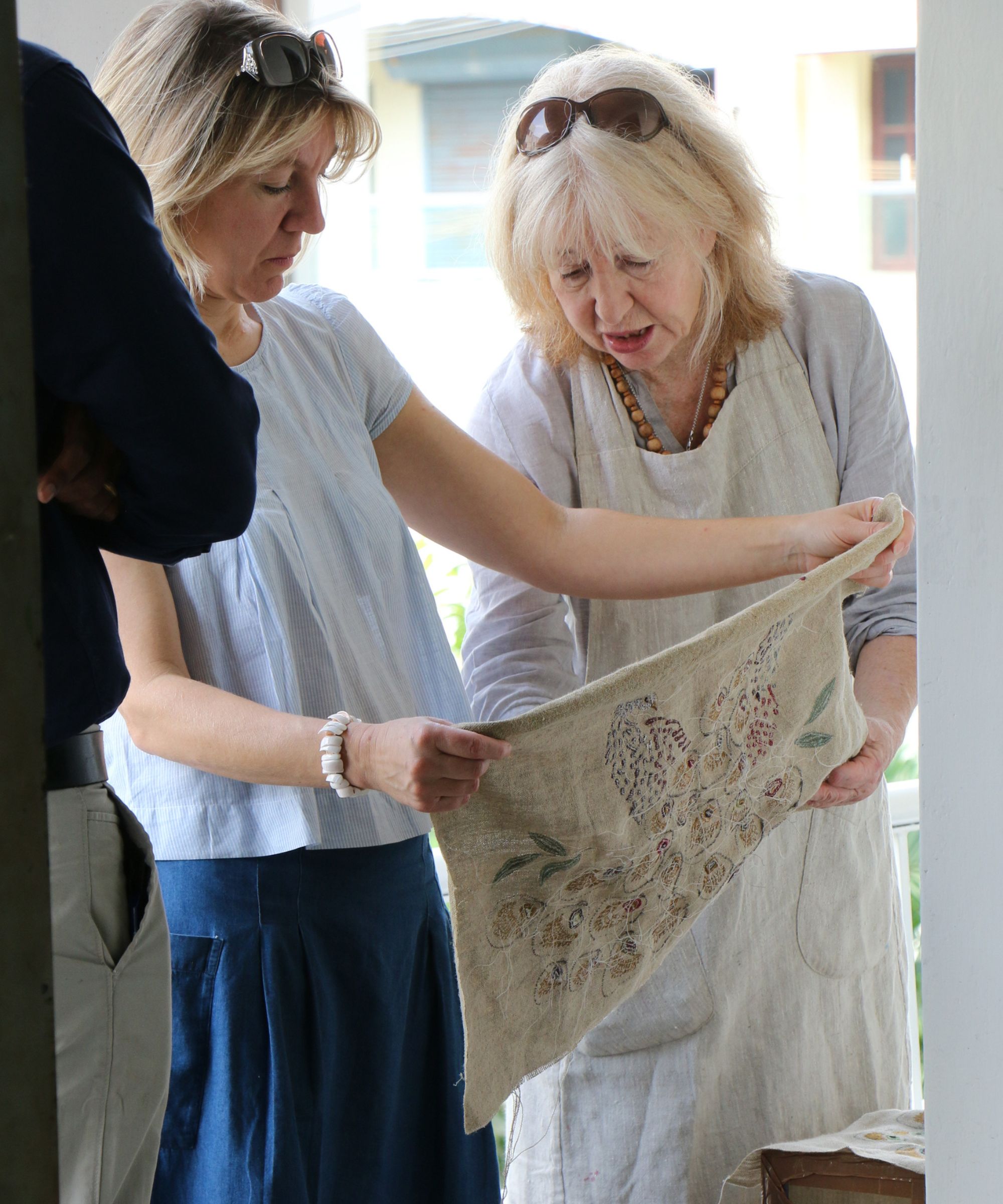 Designers Susie and Anna Watson standing together to closely inspect an intricately embroidered piece of linen fabric.