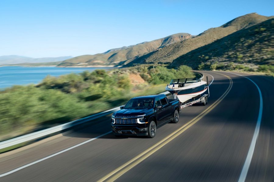 2027 Chevrolet Silverado 1500 High Country in Black. Exterior driver front 3/4 beauty shot, driving while towing. 2027 Chevrolet Silverado 1500 High Country