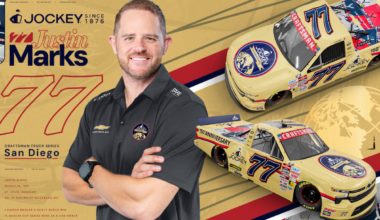 Portrait of NASCAR driver Justin Marks with two yellow race cars and Jockey branding on a gold backdrop.