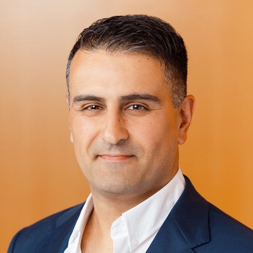 A headshot of Dr. Mypinder Sekhon in a suit with an orange backdrop.