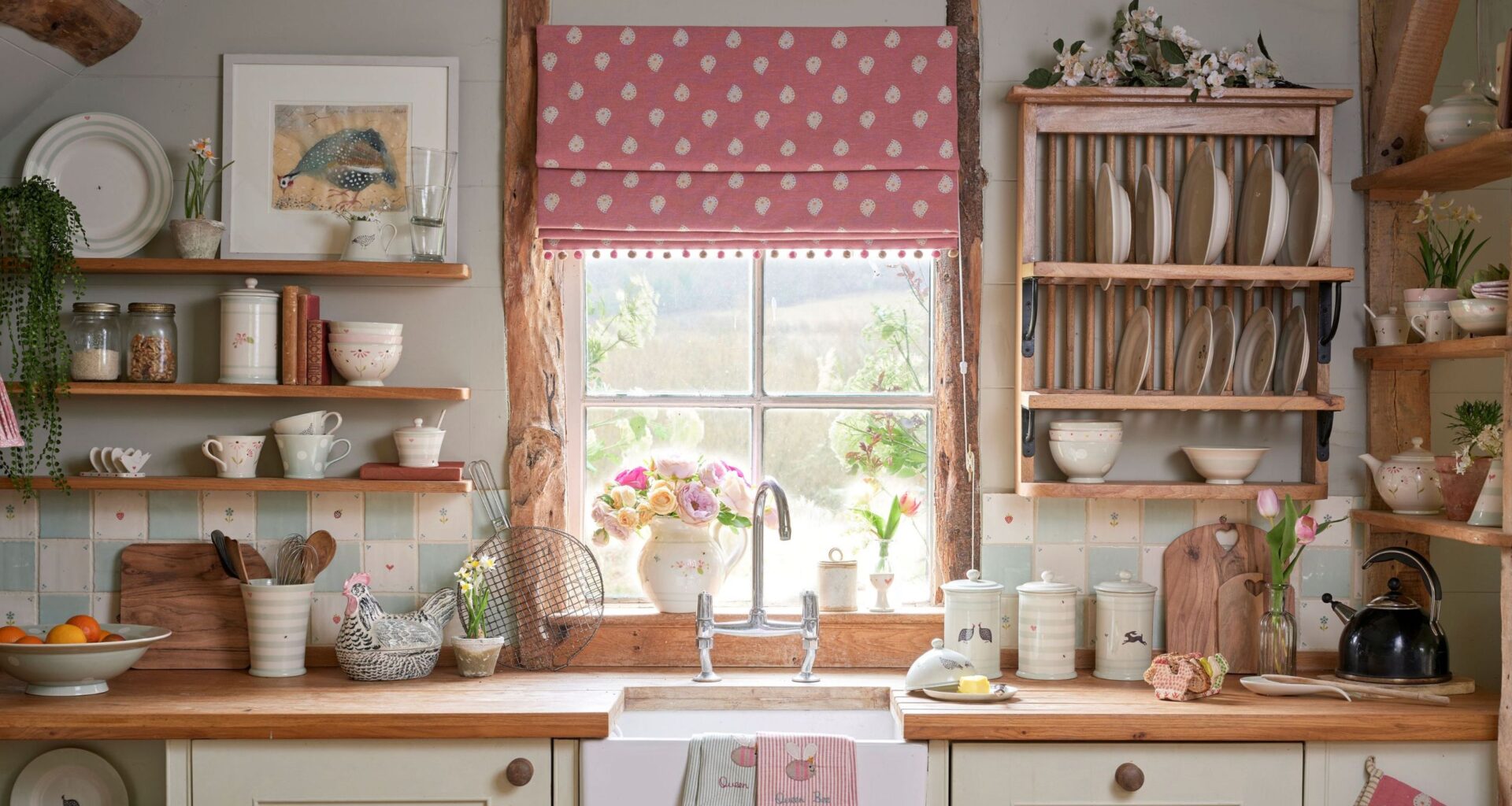 Kitchen sink beneath a window with a pink Roman blind, featuring wooden countertops, a farmhouse sink, and a wooden plate rack