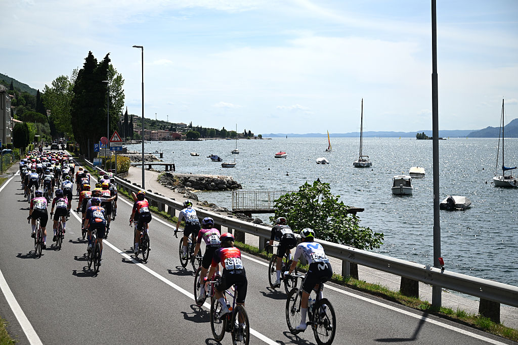 The peloton, pictured from behind, passing water on their right with sailboats