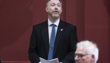 Youri Chassin stands and speaks with papers in his hands at a legislature desk.