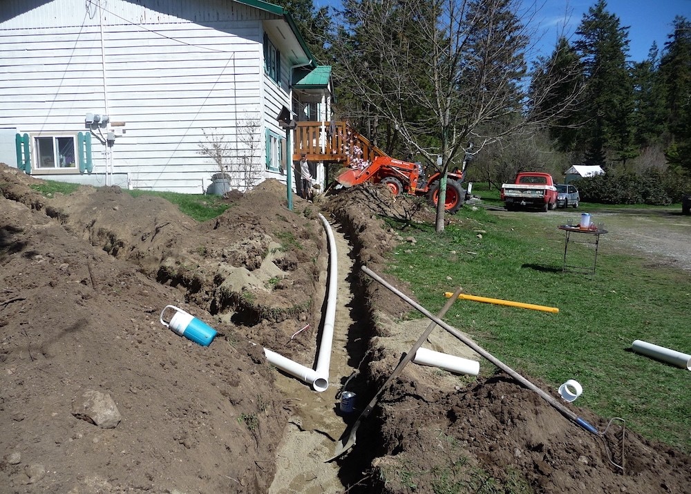 Underground pipes connect from a green metal house roof.