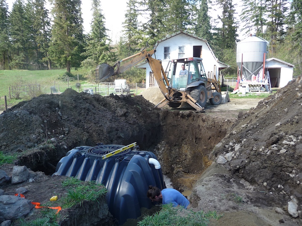 An excavator installs black water tanks underground.