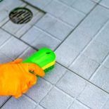 A woman cleans a bathroom toilet with a scrub brush.