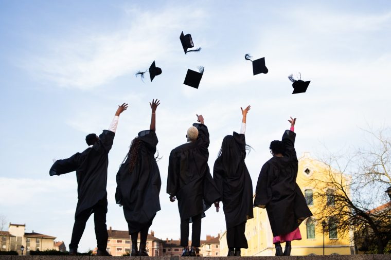 Young adults in graduation gowns joyfully tossing caps into the sky, celebrating achievement and new beginnings against a clear backdrop