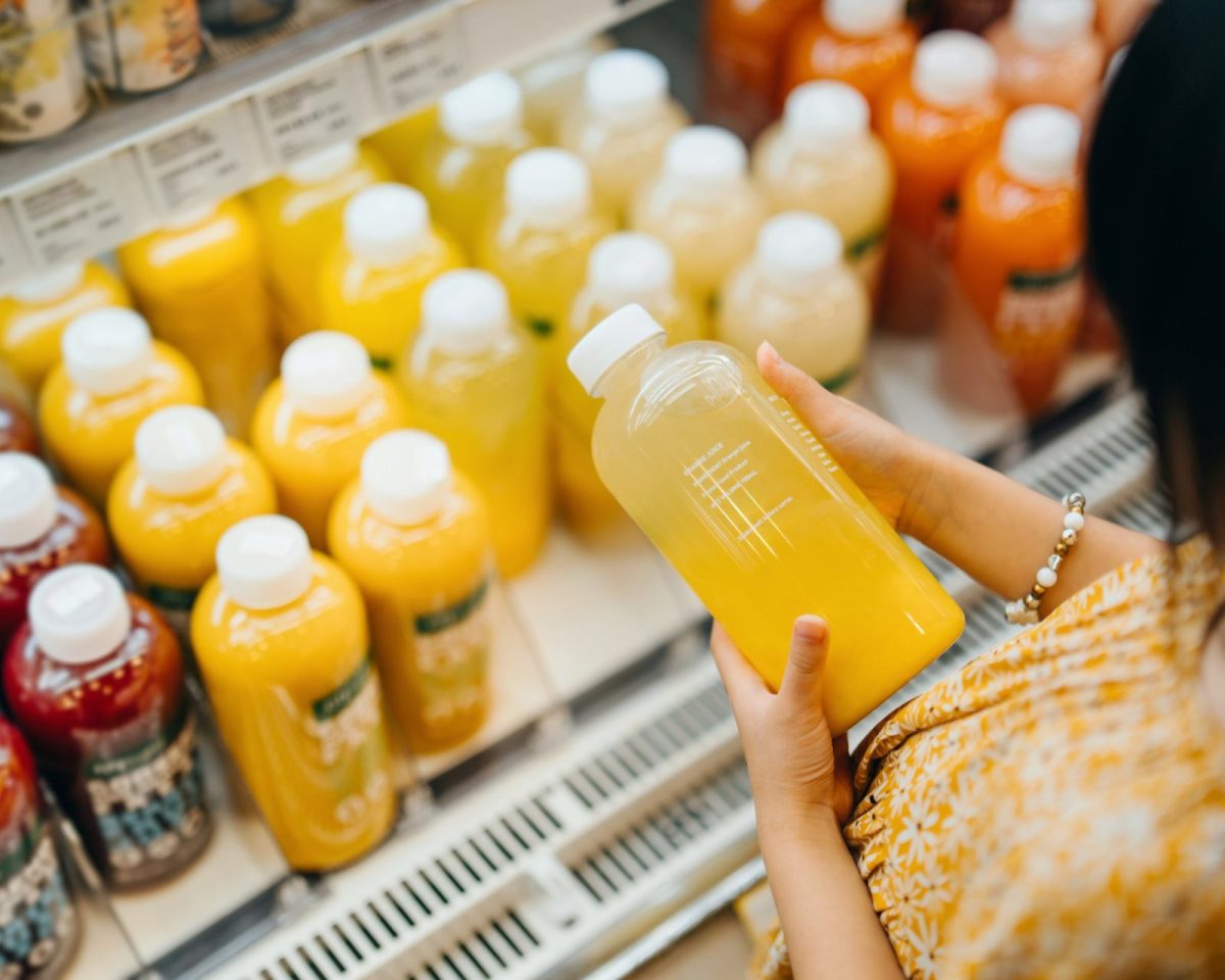 Asian girl grocery shopping in supermarket. She is choosing fresh fruit juice along the beverage aisle, reading the nutrition label and checking ingredients on the bottle. Making a healthier food choice and balanced diet. Healthy eating lifestyle