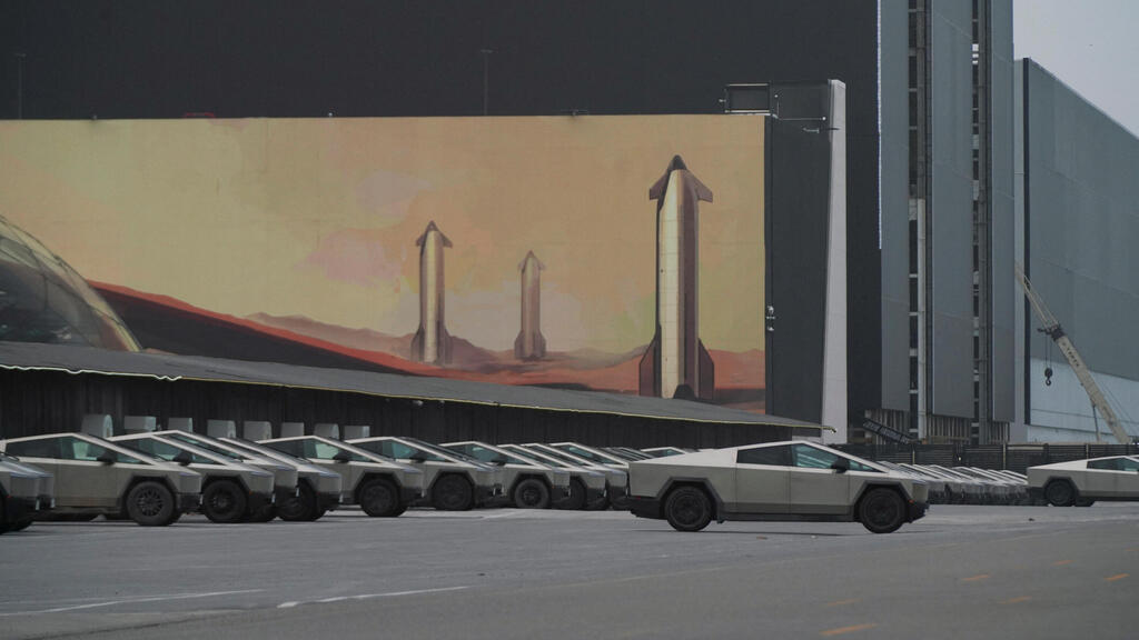 A row of Tesla Cybertrucks, with an illustration in the background depicting the vision of settling Mars (Photo: Gabriel V. Cardenas/Reuters) שורת רכבי טסלה סייברטראק, ברקע האיור שממחיש את החזון להתיישב על מאדים