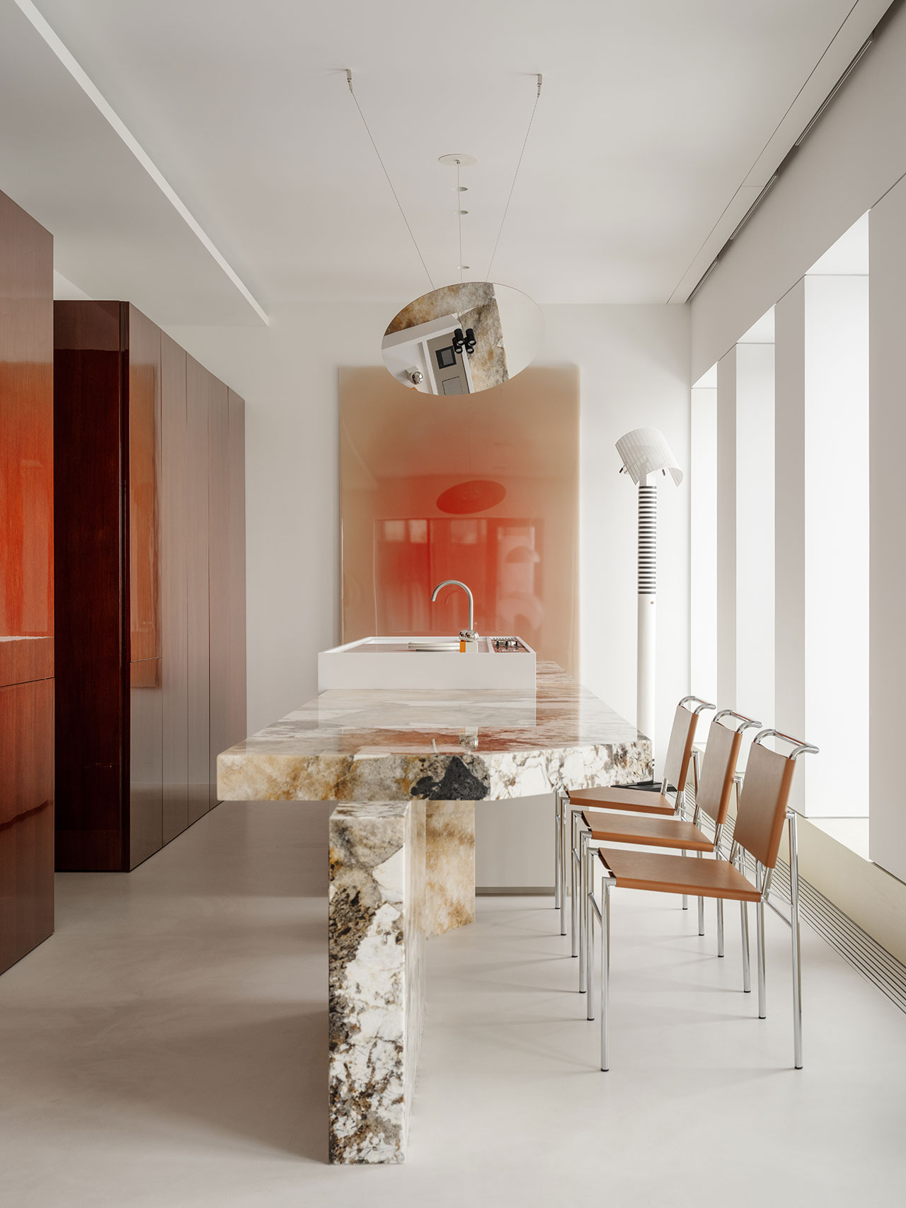 Modern Antwe kitchen featuring a stone island countertop, four tan chairs with metal frames, wall-mounted art, and minimalist lighting in a bright, minimalist space.
