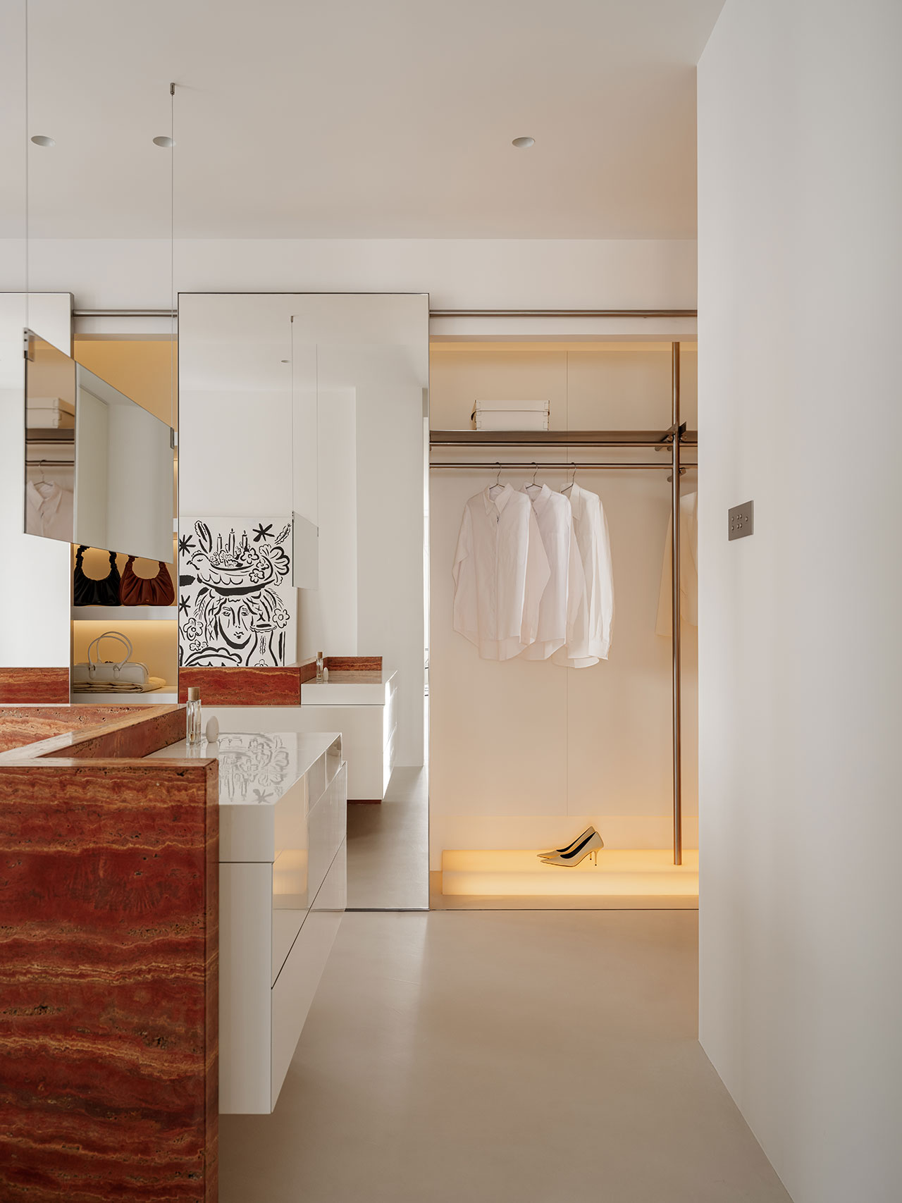 A modern Antwe closet with white shirts hanging, a single shoe on an illuminated shelf, a mirror, and a vanity featuring a striking red marble countertop.