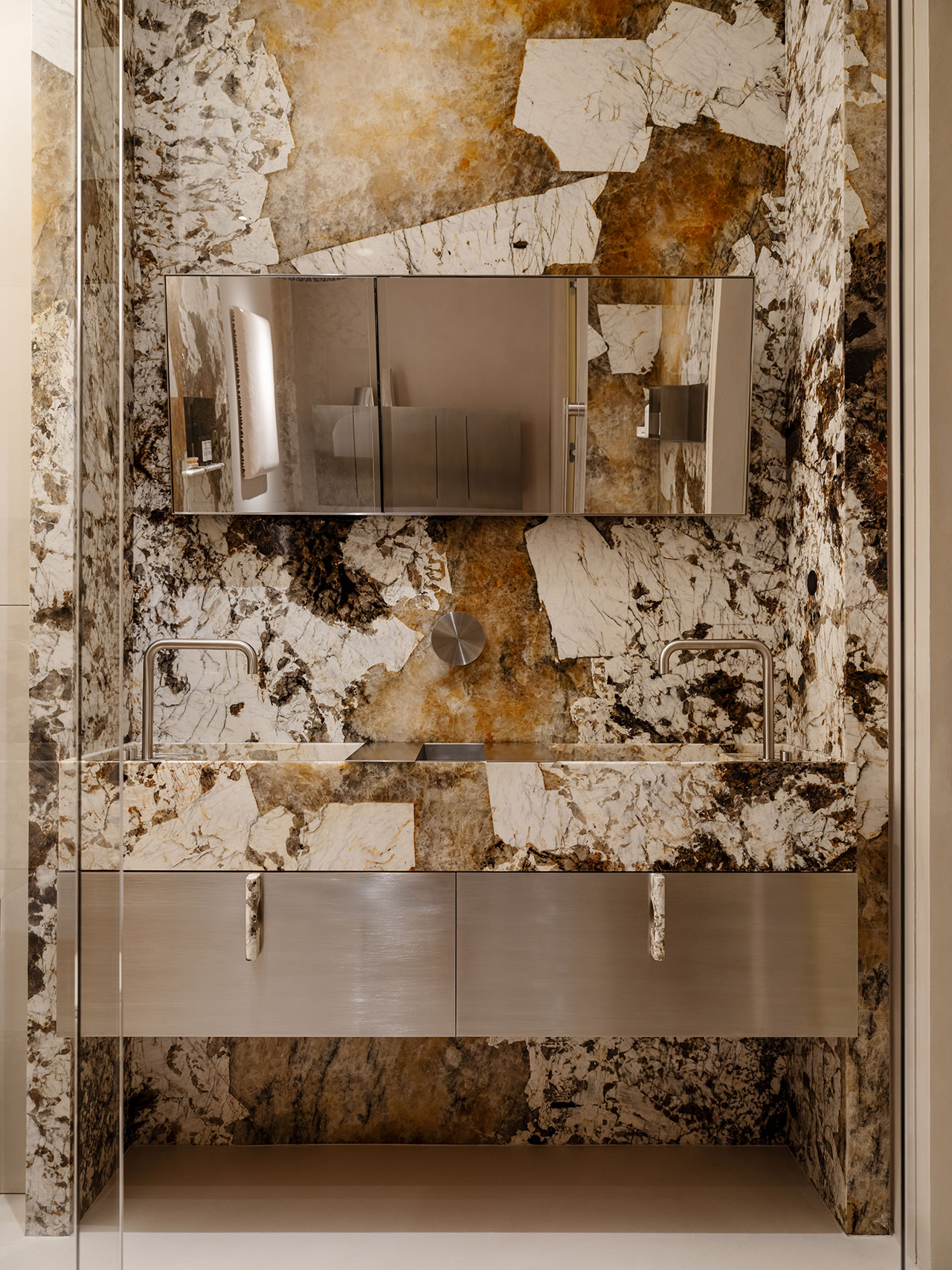 Modern Antwe bathroom with a large mirror, dual sinks, metallic fixtures, and a striking marble-patterned wall in shades of brown, white, and black.