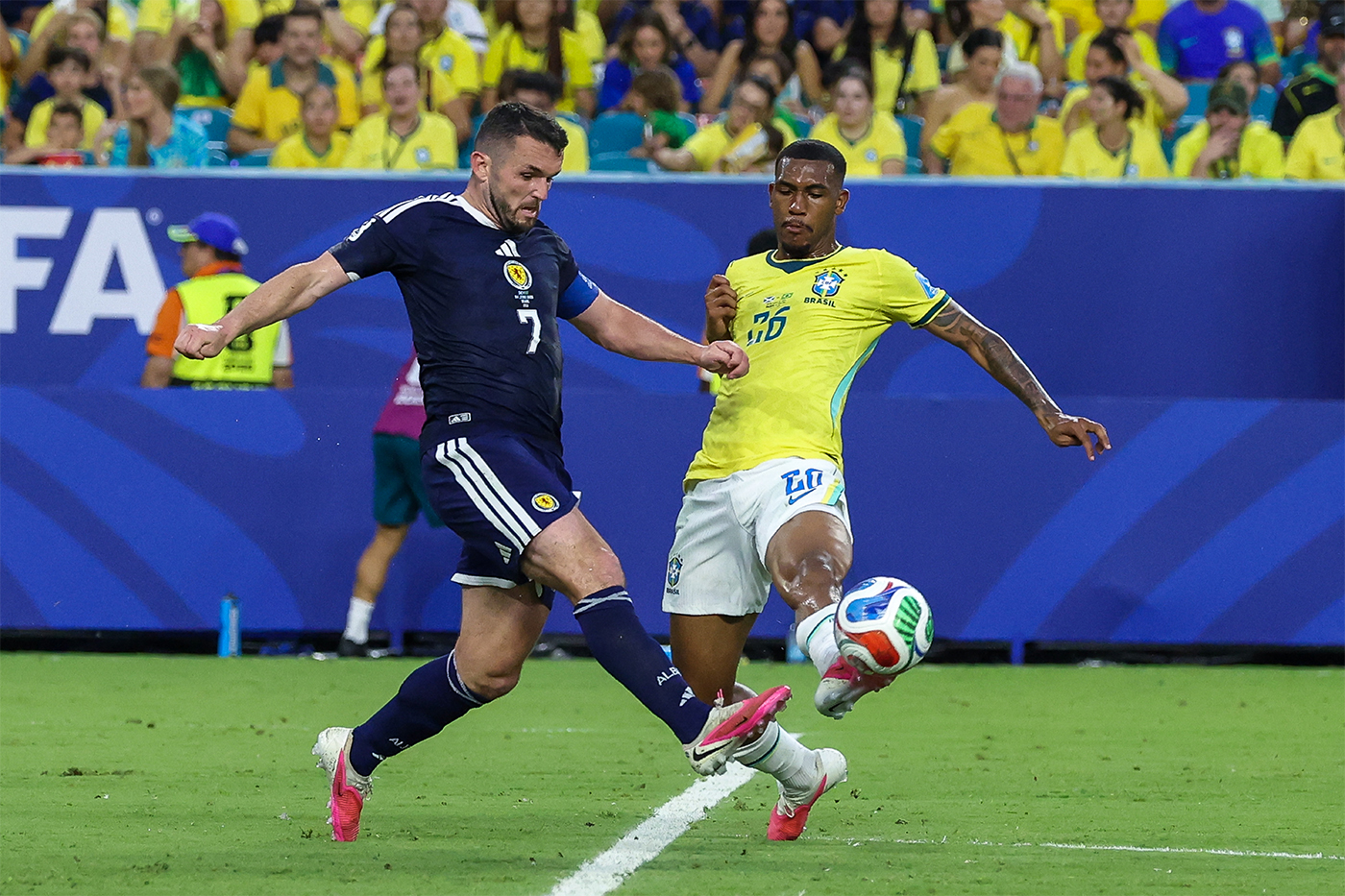 ohn McGinn #7 of Scotland and Rayan #26 of Brazil battle for the ball during a FIFA World Cup match.