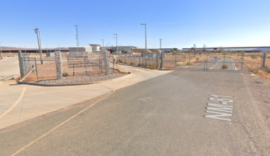Exterior view of the Antelope Wells Border Station in New Mexico, featuring a gated entrance with a sign for U.S. Customs and Border Protection. The surrounding area is arid with sparse vegetation, and the sky is clear.