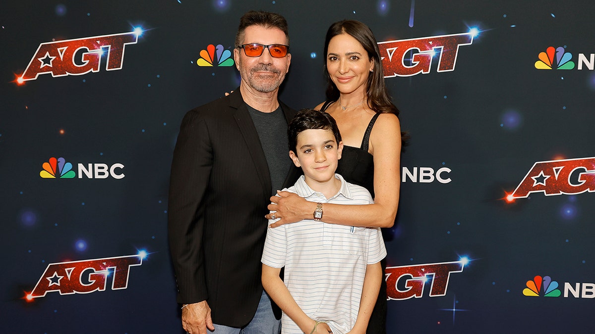 Simon Cowell standing with Eric Philip Cowell and Lauren Silverman on red carpet in Pasadena