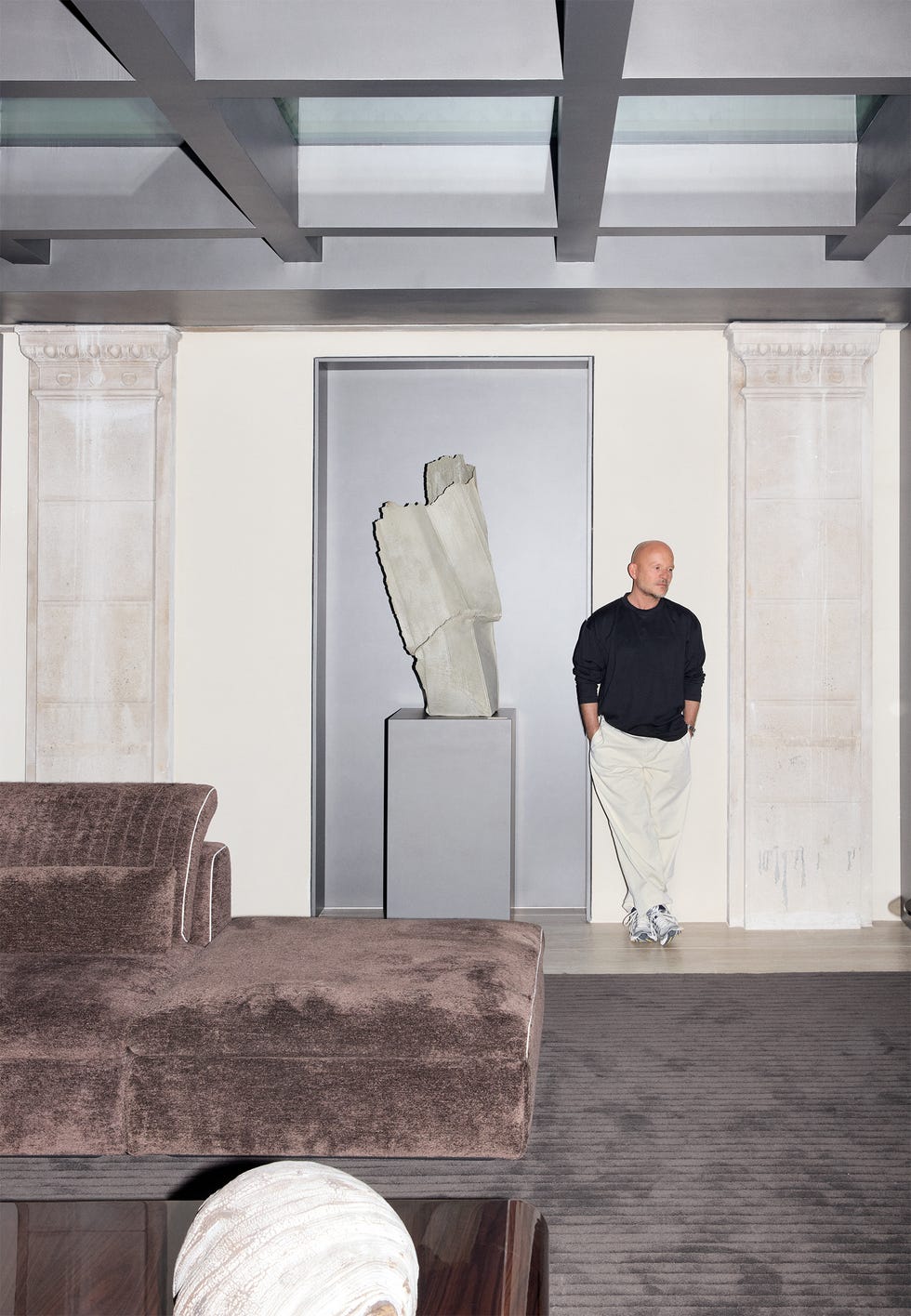 Person in modern room with abstract sculpture and plush furniture.