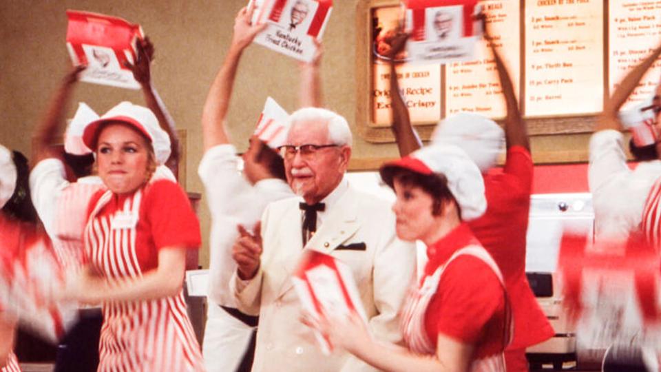 Photo of the original Colonel Sanders surrounded by KFC workers