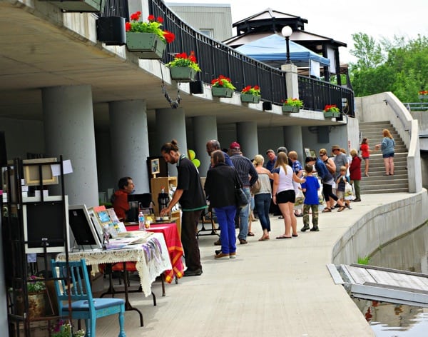 people browsing at tables of vendors near water