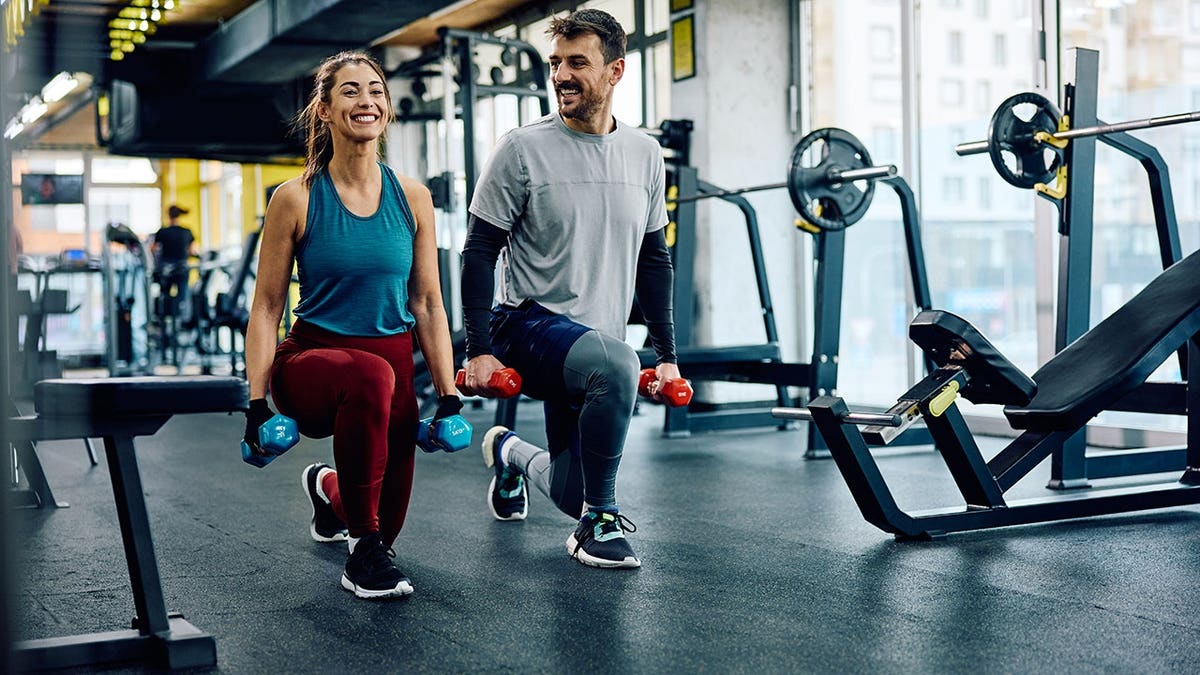 Happy athletic couple performing lunges during weight training at a health club