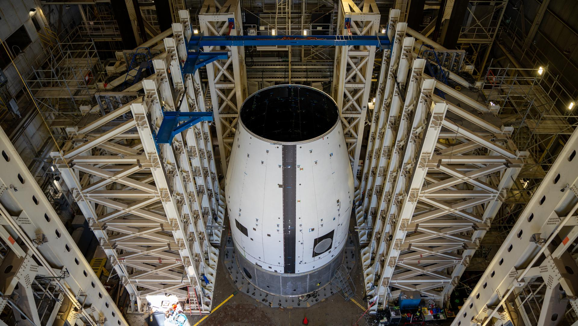 tall scaffolding surrounds a white, conical structure in a hangar-like room.