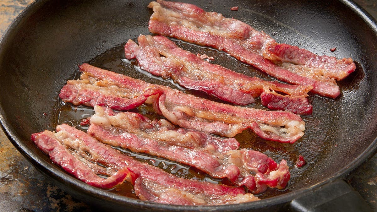 Five strips of bacon sizzle in a frying pan.