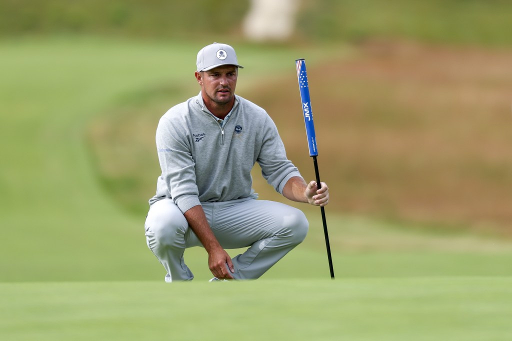 Bryson DeChambeau of the US crouches down on the golf course, preparing to putt, during the 2026 US Open golf tournament.