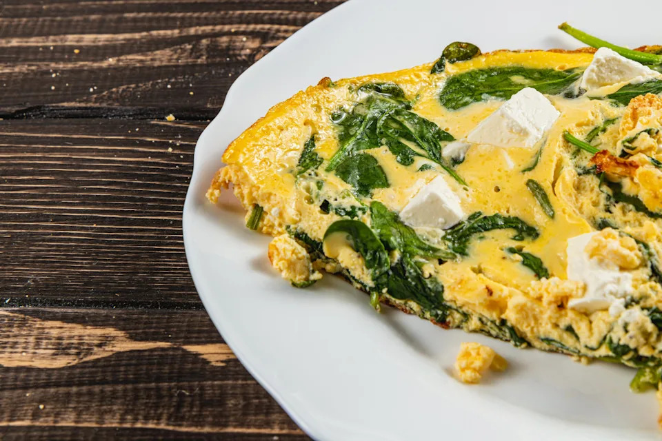 Omelet with spinach and feta cubes on a white plate, on a wooden table