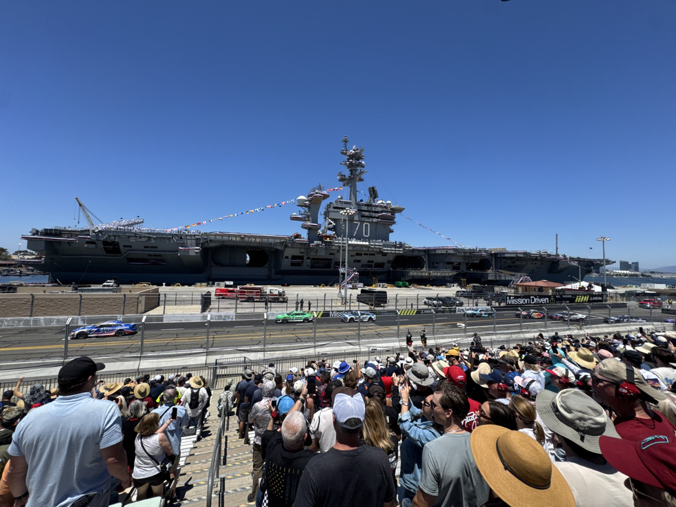 aircraft carrier docked with a crowd watching a racing event