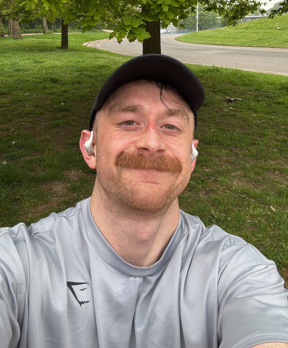 person in a gray shirt with earbuds in a park setting