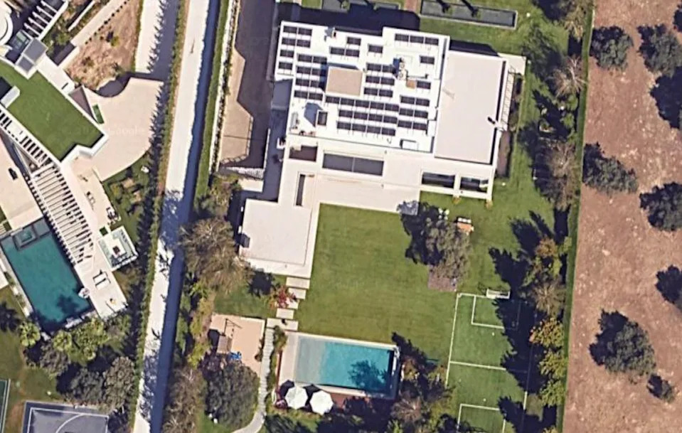 Aerial view of a modern house with solar panels, a pool, and a garden area with trees.