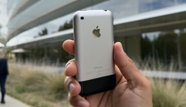 A hand holding up the original iPhone outside Apple Park