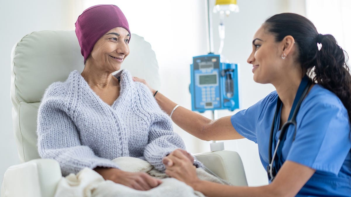A senior woman with a headscarf sitting in a high back chair talking with her nurse during chemotherapy treatment