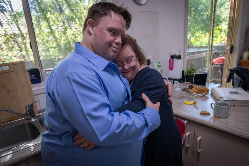 A married couple embrace in the kitchen of a suburban house.